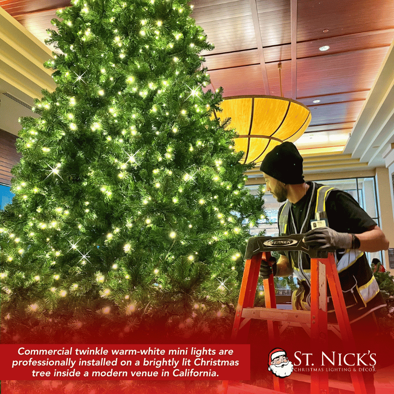 Installer works beside a large indoor Christmas tree densely illuminated with warm white mini lights in Valley Center, California.