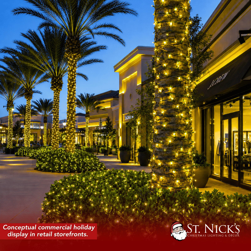 Conceptual retail plaza with palm trunks and shrubs illuminated by yellow mini lights beside storefronts and walkways.