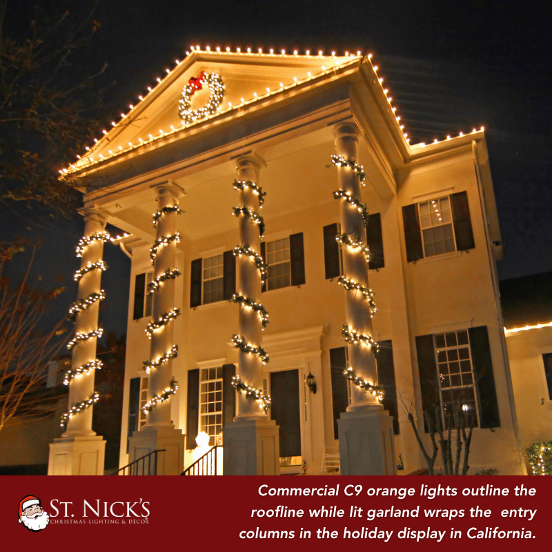 Orange C9 lights outline a building roofline while illuminated garland spirals around entry columns in a California holiday display.