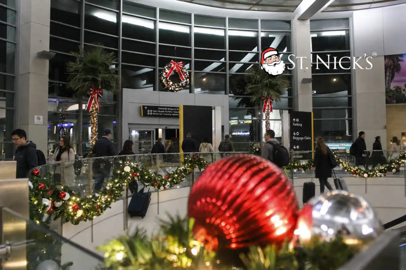 Commercial Christmas garlands, illuminated wreaths, red bows, and warm white lights decorating an airport terminal.