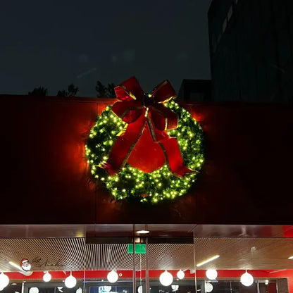 Decorative Christmas wreath with a red bow on a building at night.