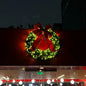 Decorative Christmas wreath with a red bow on a building at night.