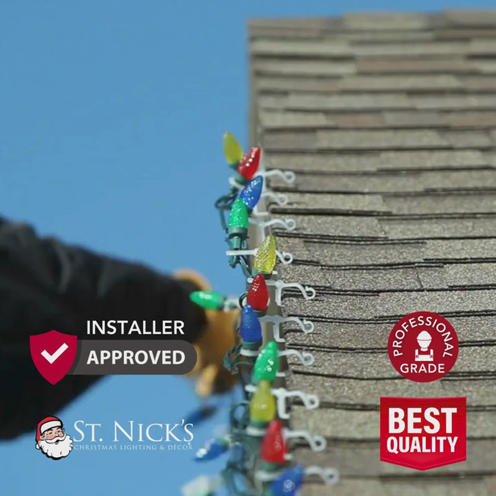 Installer attaches colorful C9 Christmas lights along a shingle roofline with professional-grade lighting badges displayed.