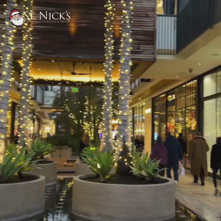 Video tours a shopping center where palm trunks are wrapped in warm white LED mini lights beneath illuminated garland.