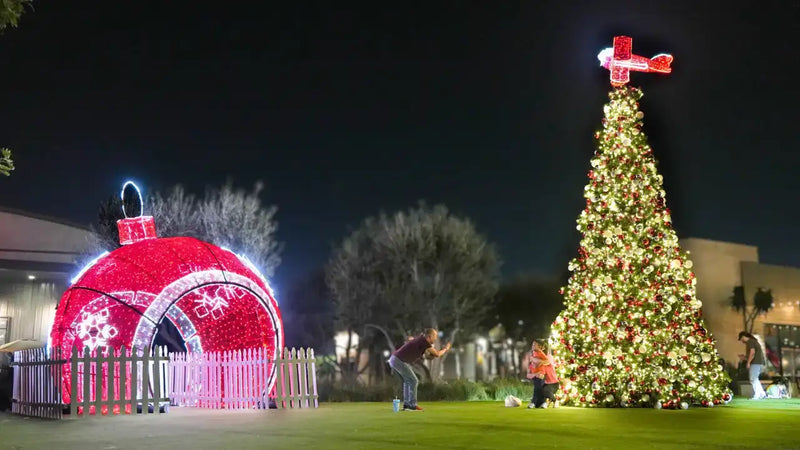 Decorative Christmas scene with a large lit-up tree and a red and white str walkthrough in a park setting.